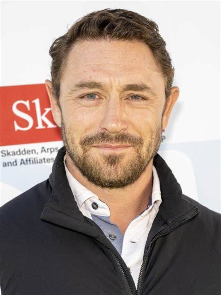 JJ Feild in a light brown jacket and red cap holding his baby with his wife in a blue tops.