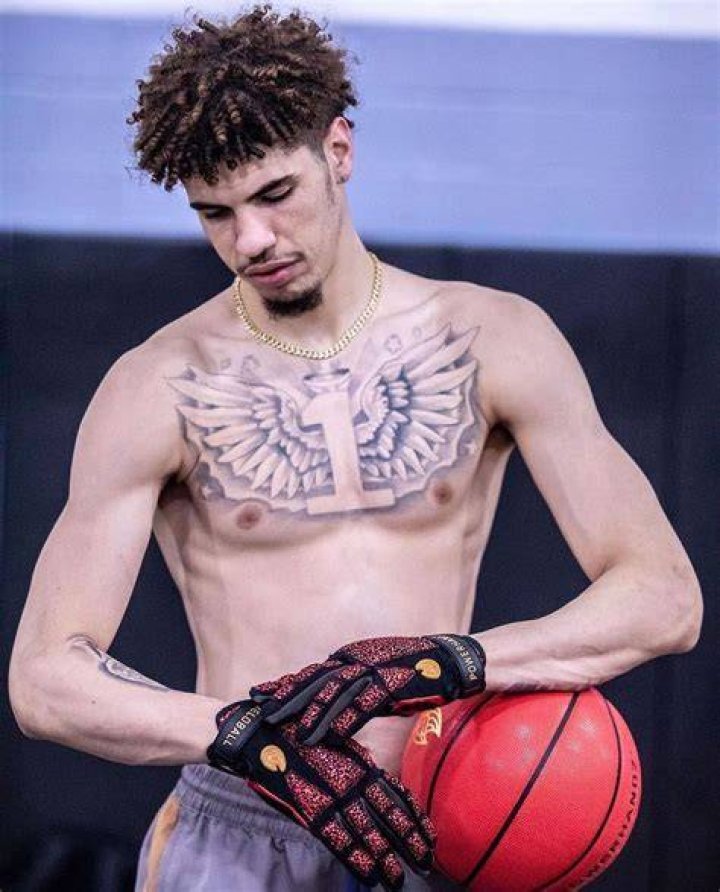 LiAngelo Ball showing his tattoo with his pet. He is wearing a black woolen cap, black sweat pant and white shoes.